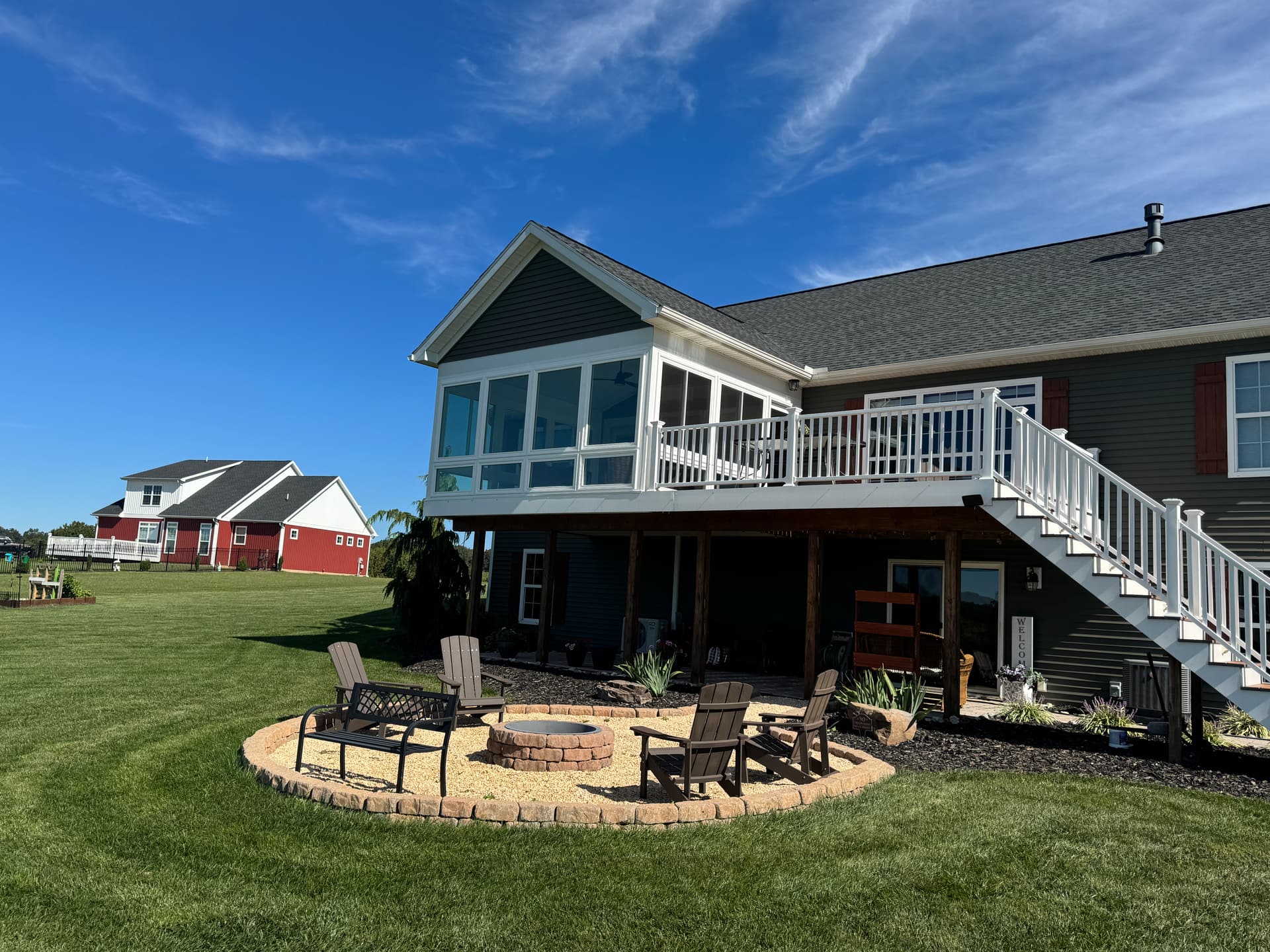 Sunroom addition built above a deck with white railings and stairs, overlooking a backyard fire pit patio