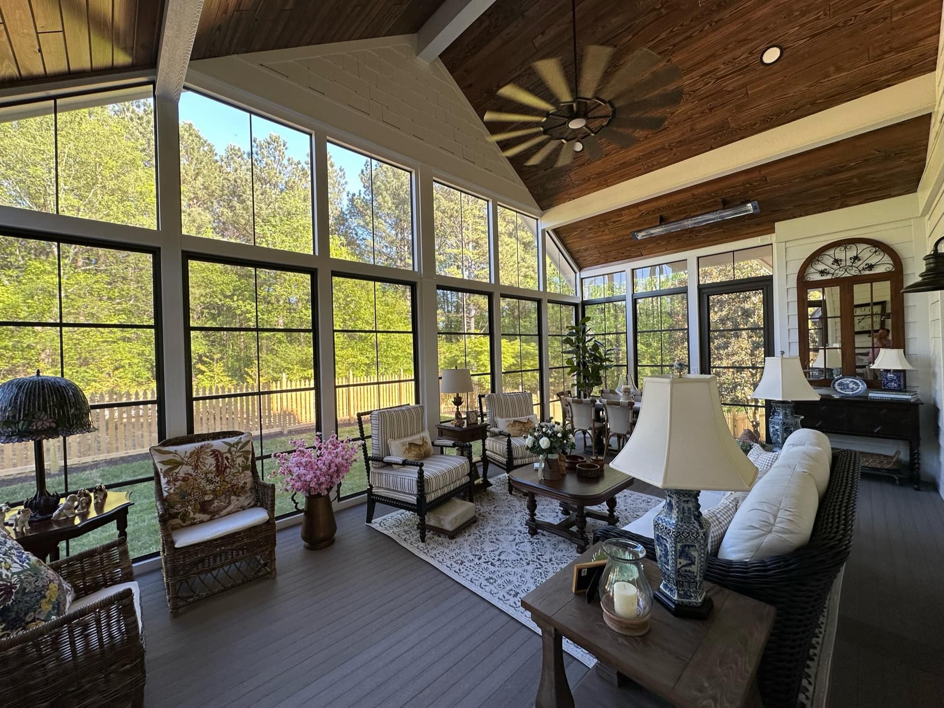 Sunroom interior with a vaulted wood ceiling, floor-to-ceiling black-framed windows, and wicker seating